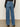 A person stands on a neutral background facing away, showcasing the back pockets of the Sanctuary Clothing tuxedo relaxed straight jean flirt paired with a long-sleeve black top.