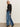 A woman with straight blonde hair and a neutral expression stands against a plain background, wearing Sanctuary Clothing„¢s tuxedo relaxed straight jean flirt with a dark blue side stripe, paired with a black lace top, black belt, and black boots.