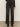 A person wearing Sanctuary Clothing's tuxedo relaxed straight jean black tie with a textured black long-sleeve top and heeled boots, standing against a plain light background.