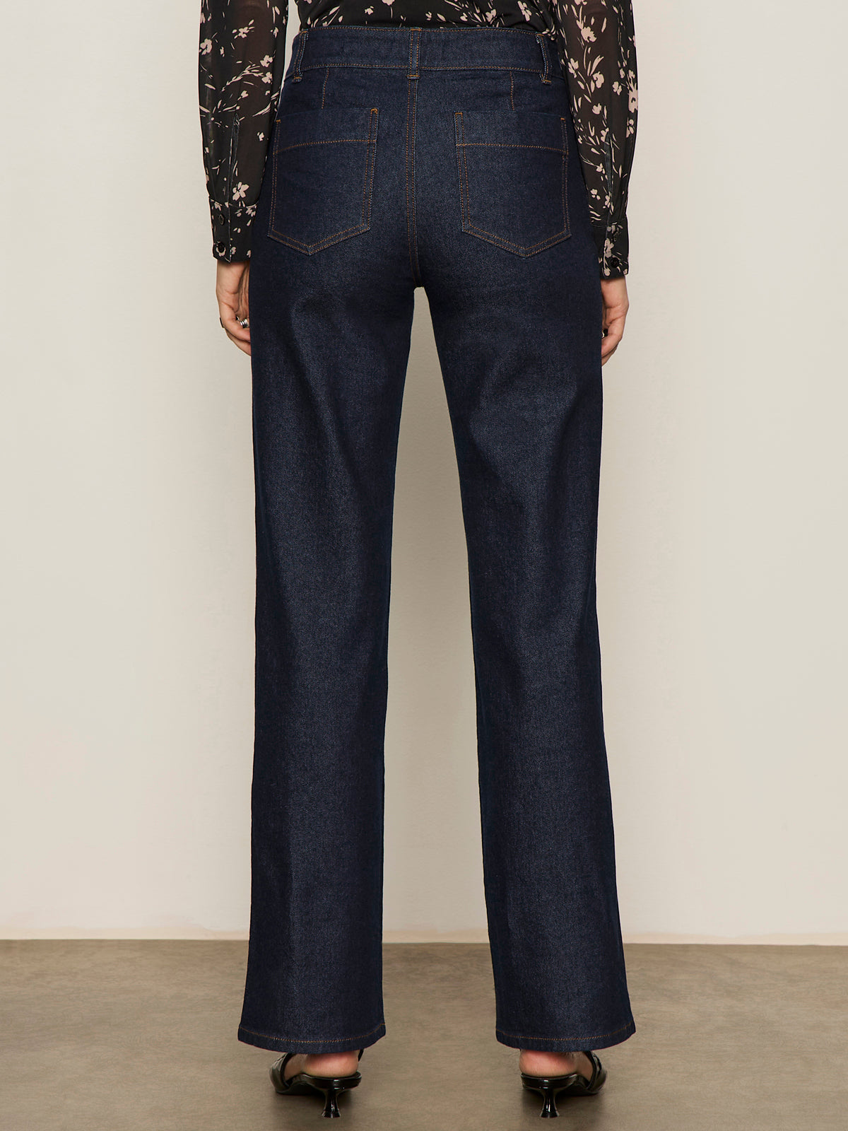 A person wearing Sanctuary Clothing„¢s marine full length jean first sight, shown from the back, stands on a light brown floor against a neutral wall.