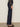 A person stands sideways in Sanctuary Clothing's marine full length jean first sight, paired with a black floral long-sleeve blouse and black slingback heels against a plain light background.