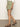A person stands against a plain background in a white shirt, Sanctuary Clothing's all buttoned up skirt in sage, and brown sandals. Their right arm displays a bracelet, with bare legs visible.