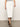 A person is wearing a Sanctuary Clothing carrier denim skirt in bleached white, paired with a black and white striped top. They stand on a neutral floor wearing black sandals and have a simple ring on their right hand; their head is not visible.