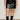 A person wears Sanctuary Clothing's camden skirt black extended sizing with black mid-calf buckle boots and a white top, standing against a light background for a modern, edgy look.