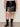 A person wears Sanctuary Clothing's camden skirt black extended sizing with black mid-calf buckle boots and a white top, standing against a light background for a modern, edgy look.