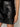 A close-up of a person wearing the Sanctuary Clothing camden skirt black—a shiny, smooth faux leather skirt with front pockets—paired with a black top, one hand resting by their side.