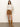 A woman stands against a plain background wearing a cream knit sweater, tall brown suede boots, and the Sanctuary Clothing briar corduroy mini skirt in bronze, with one hand in her skirt pocket.