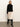 A woman stands against a light background wearing a black long-sleeve sweater, black knee-high heeled boots, and the Sanctuary Clothing evermore pleated midi skirt in light oat with a black lace hem.