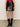 A person is seen from the waist down wearing the Sanctuary Clothing broadway leather skirt in black, paired with black patent boots and a red top, standing against a plain light-colored wall.