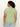 A person with curly hair and hoop earrings, facing away, wears light blue jeans and a green short-sleeve shirt from Sanctuary Clothing's "the perfect tee mosaic inclusive collection" featuring a white paisley pattern.