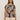 A woman wears Sanctuary Clothing's "the perfect tee mesa palm extended sizing," a short-sleeve beige top with dark brown palm leaves, paired with light beige shorts, standing against a plain, light background.