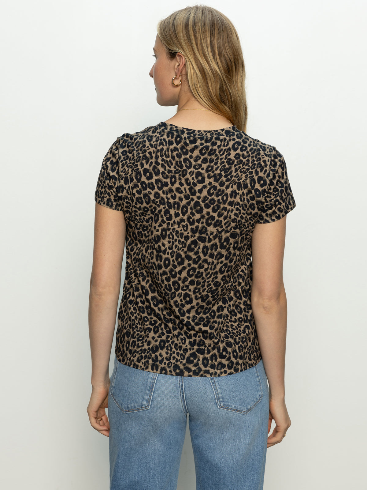 A woman with long, light brown hair faces away, wearing Sanctuary Clothing's "the perfect tee french kitty" and light blue jeans against a plain white background.