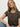 A woman with long blonde hair wears the Sanctuary Clothing "the perfect tee french kitty" t-shirt and blue jeans, accessorized with a gold necklace, sitting against a plain light background and looking confidently at the camera.