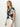 A person with long blonde hair stands against a light background, wearing Sanctuary Clothing's "the perfect tee inked impressions" and white pants. They look to the side with a relaxed expression.
