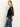 A woman with long, straight blonde hair stands in profile with hands in her pockets, wearing Sanctuary Clothing's black long sleeveperfect mesh tee and blue jeans against a plain light background.