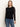 A woman with straight, light brown hair wears the Sanctuary Clothing long sleeveperfect mesh tee in black�featuring fitted sheer sleeves�paired with blue jeans, and stands against a plain light background.