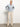 A person stands confidently against a plain background, donning the Quilted Button Up Popover Top in Pearl Blue by Sanctuary Clothing, paired with beige pants and light-colored shoes. Their hands rest on their hips as they gaze slightly upward.