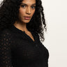A woman with long, curly dark hair wears the Sanctuary Clothing dreamgirl lace button up black top, looking at the camera against a plain light background.
