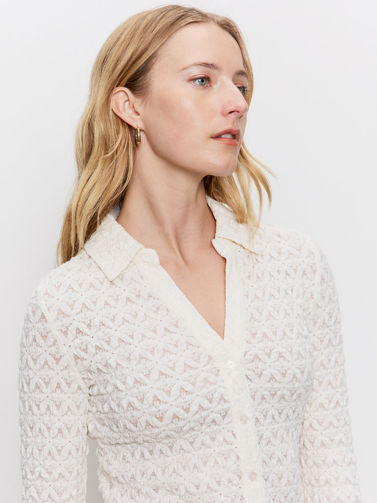 A woman with long blonde hair wears the Sanctuary Clothing dreamgirl lace button up chalk blouse and gold hoop earrings, looking to the side against a plain white background.