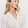 A woman with long blonde hair wears the Sanctuary Clothing dreamgirl lace button up chalk blouse and gold hoop earrings, looking to the side against a plain white background.