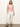 A person with long hair wears the Sanctuary Clothing draped tank in cherry blossom and white cropped pants, standing against a plain light background with hands in pockets and wearing brown sandals.
