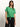 A person with long brown hair stands against a neutral background, wearing a Sanctuary Clothing all day eyelet tee in palm, tied at the waist, and black pants. They sport a necklace and look confidently forward.