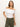 A woman models the Sanctuary Clothing off-shoulder rib tee in white, paired with olive green pants. She has long hair and looks at the camera with a slight smile against a plain background.