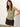 A person with long brown hair wears Sanctuary Clothing's ribbed ruched tank in sage and black shorts, standing against a plain white background with one hand on their hip, confidently gazing at the camera.