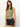 A woman with long brown hair wears a Sanctuary Clothing ribbed ruched tank in sage and black shorts, accessorized with layered necklaces. She stands against a plain white background with a relaxed and confident expression.
