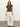 A woman with long brown hair stands against a white background, wearing a Sanctuary Clothing embroidered perfect tee in kalamata, light beige wide-leg pants, black sandals, and layered necklaces. One hand rests on her hip.