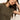 A woman with long brown hair rests her head on her hand, wearing Sanctuary Clothing's embroidered perfect tee in kalamata, gold necklaces, and hoop earrings. She gazes softly to the side against a plain background that highlights her relaxed pose and attire.