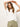 A woman with long, wavy hair poses with her eyes closed and arms raised in front of a plain white background. She's wearing Sanctuary Clothing's embroidered perfect tee in white paired with light green pants.