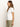 A woman with long brown hair is standing in profile against a plain background, wearing an embroidered perfect tee white by Sanctuary Clothing and olive green pants.