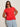 A woman wears the Sanctuary Clothing knotted muscle tee in cayenne (extended sizing) with light blue jeans. She stands against a light wall, has long brown hair, sunglasses, and her hands are behind her back.
