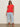 A woman wearing Sanctuary Clothing's knotted muscle tee in cayenne, light blue wide-leg jeans, sunglasses, and beige slide sandals stands against a plain beige background.
