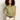 A woman with curly hair models the Sanctuary Clothing knotted muscle tee bamboo in light green, paired with beige pants and a brown belt, posing against a plain light background with one hand on her hip.