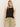 A person with long blonde hair stands against a plain backdrop, wearing Sanctuary Clothing's linen tank in black, paired with light brown drawstring pants.