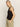 A person with long blonde hair stands sideways, looking at the camera with a neutral expression. They wear the sleeveless "linen tank black" by Sanctuary Clothing and light olive green pants with pockets. The background is plain and light-colored.