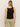 A person with long blonde hair is facing away, wearing Sanctuary Clothing's black linen tank and khaki pants with visible back pockets, standing against a plain beige background.