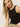 A woman with long blonde hair wears a Sanctuary Clothing linen tank in black, paired with beige pants, and looks towards the camera against a neutral background.