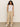 A person with curly hair is standing against a plain background, dressed in Sanctuary Clothing's linen tank in white and beige wide-leg pants, with one hand in their pocket and wearing white sneakers.