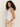 A person with curly hair models the ˜linen tank white™ from Sanctuary Clothing, posing sideways against a plain background in beige pants, with one hand in their pocket and looking at the camera.