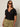 A woman with long brown hair wears sunglasses and the Sanctuary Clothing notch neck tee in black extended sizing, paired with light olive drawstring pants, standing against a plain light background.