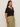 A person with long brown hair wears the Sanctuary Clothing notch neck tee in black (extended sizing) and loose-fitting olive green drawstring pants, standing against a plain light background and looking slightly to the side.