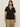 A woman with long brown hair wears the Sanctuary Clothing notch neck tee in black (extended sizing), paired with light olive green pants, standing against a plain, light-colored background.