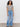 Against a plain background, a woman with curly hair and a relaxed, confident posture wears the Sanctuary Clothing notch neck tee light oat black stripe 2, paired with light blue wide-leg jeans and black sandals.