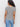 A woman with curly hair is shown from the back wearing the Sanctuary Clothing notch neck tee light oat black stripe 2 and light blue jeans, standing against a plain white background.