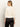 A woman with straight, light brown hair is seen from behind wearing the relaxed sparkle popover chalk sweater by Sanctuary Clothing and black satin pants, set against a plain light background.
