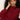 A woman with curly hair wears the Sanctuary Clothing change of pace top in crimson, sitting thoughtfully with her hand to her head against a plain light background.