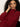 A woman with curly hair wears the Sanctuary Clothing change of pace top in crimson, sitting thoughtfully with her hand to her head against a plain light background.